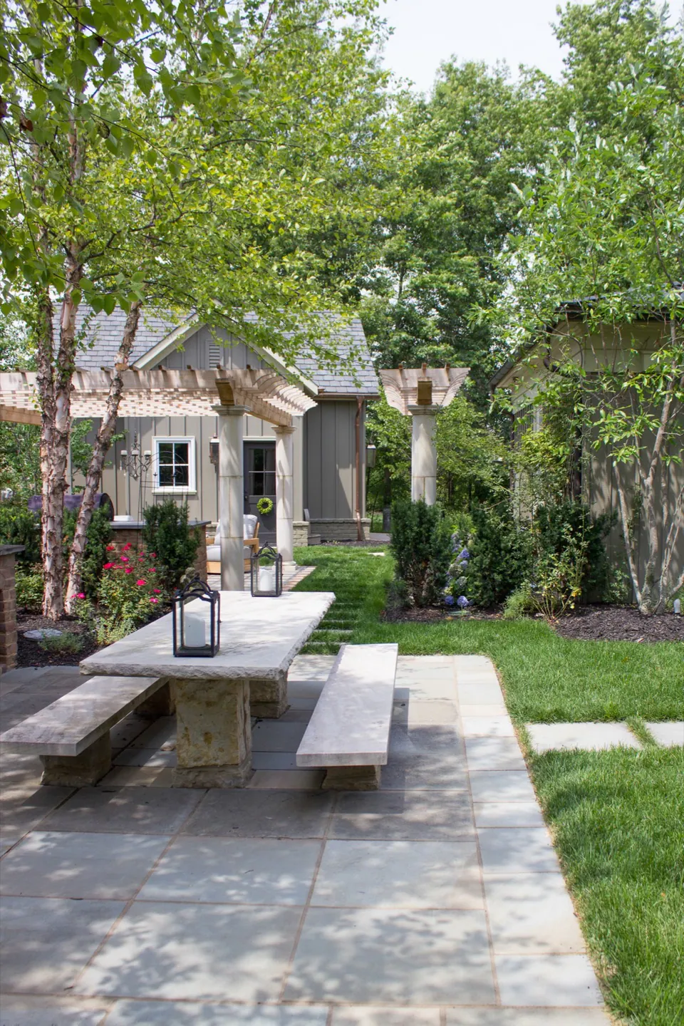 Large rectangular stone pads and lawn panels leading between fireplace seating and pergola kitchen in a formal backyard garden.